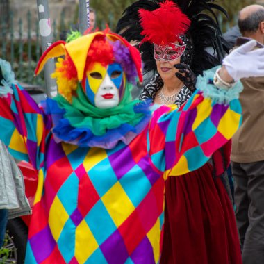 Canlı bir sokak kutlaması sırasında renkli kostümler, maskeler ve şapkalar içinde şenlikli figürler..