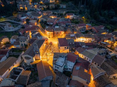 Tepelere kurulmuş büyüleyici bir Avrupa köyünün havadan görünüşü, alacakaranlıkta sıcak ışıklarla aydınlanıyor..