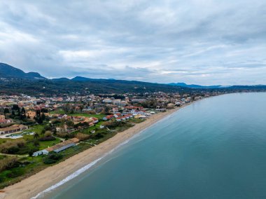 Kumlu sahili, yeşil manzarası ve bulutlu gökyüzünün altındaki dağları olan bir sahil kasabasının havadan görünüşü..