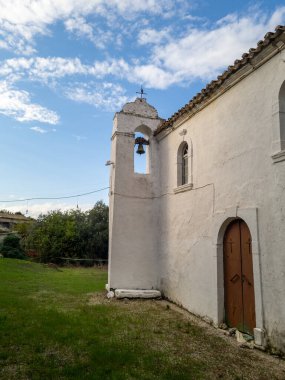 Kemerli bir kapı aralığı, öne çıkan bir çan kulesi ve parçalı bulutlu bir gökyüzünün arka planının yer aldığı eski, beyaz yıkanmış bir kilisenin dış perspektifi..