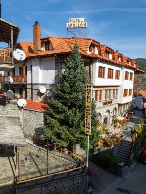 Çekici bir otelin dış görünüşü, taş aksanlar, terracotta çatıları, ve mavi gökyüzüne karşı kurulmuş, sakin bir manzara yaratıyor..