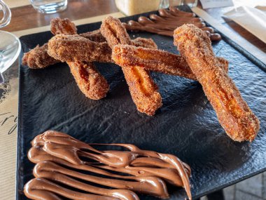 Şekerli ve tarçınlı lezzetli altın sarısı churro, kalın çikolata çizgileriyle kaplı, daldırmak ve tadını çıkarmak için mükemmeldir..