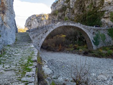 Kayalık bir nehir yatağının üzerinde, engebeli uçurumların arasına kurulmuş eski bir taş köprü yükseliyor. Taş bir merdiven köprünün tarihi yoluna çıkıyor..