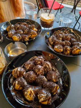Çikolata şurubuyla kaplanmış yakın çekim Loukoumades tabakları, açık havada, masada su ve kahve içeceklerinin yanında servis edilir..