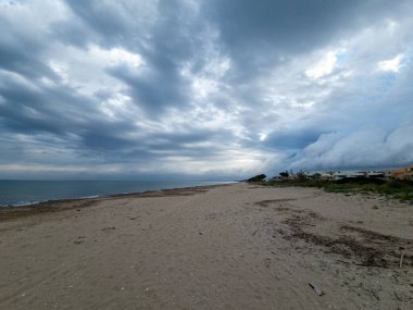 Bu görüntü bulutlu bir gökyüzünün altında, ağaçların arasına yerleşmiş, huzurlu bir kaçış sunan sakin bir kumsal yakalıyor..