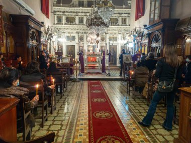 Büyük, süslü bir kilisede, insanlar ayin için toplanır, ellerinde mumlar tutarlar. İçerisi zengin bir şekilde dini sanatla süslenmiş..