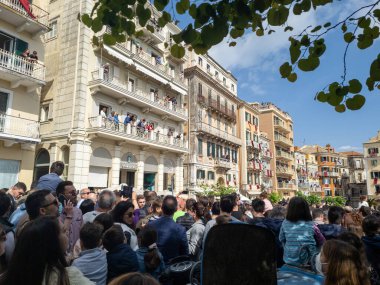 Avrupa 'da bir kasaba meydanında toplanan kalabalık, açık mavi gökyüzünün altında balkonlar inşa eden izleyiciler tarafından izleniyor..