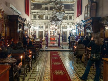 İnsanlar ellerinde mumlarla süslü bir kilisede ayine katılıyorlar. Mekanda avizeler, tablolar ve zengin ahşap işçiliği var..