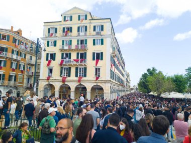 Kasaba meydanında toplanan kalabalık, binalar pencerelerden ve balkonlardan sarkan kırmızı bayraklarla süslenmiş..