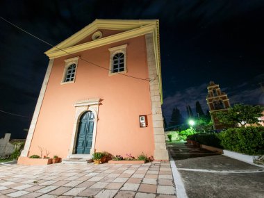 Şeftali renkli bir bina geceleri taş aksanları, koyu mavi bir kapı ve yıldızlı gökyüzünün altında görünen bir kuleyle aydınlanıyor..