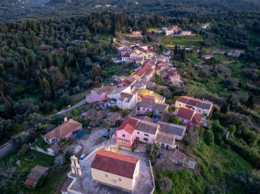 Manzaralı bir hava manzarası, yeşil ağaçlar ve dolambaçlı yollarla çevrili renkli evlerini gösteren bir tepe köyünü yakalıyor..