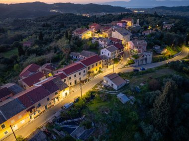 Yükseltilmiş bir çekimde canlı bitki örtüsü içinde büyüleyici bir köy sergileniyor. Yapılar dingin bir alacakaranlıkta ışıldıyor..