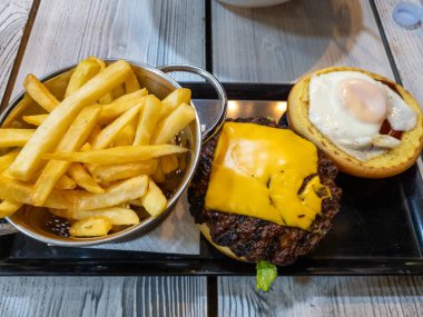 Cazip bir burger, peynirli, sulu yumurta ve yanında kızarmış patates tabakta sunuluyor. Lezzetli bir yemek olarak sunulmaya hazır..
