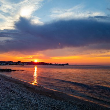 Sahil şeridi görünen sakin bir okyanusun üzerinde gün batımının güzel, manzaralı görüntüsü. Gün batımı çok güzel ve sakin..