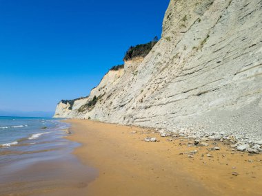 Manzaralı bir manzara, berrak okyanus sularının yanında altın kumlu bir sahili yakalıyor, yüksek katmanlı uçurumlarla çevrelenmiş, canlı mavi bir gökyüzü zeminine karşı..