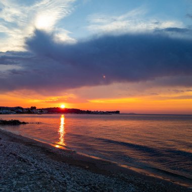 Sahil şeridi görünen sakin bir okyanusun üzerinde gün batımının güzel, manzaralı görüntüsü. Gün batımı çok güzel ve sakin..
