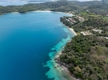 Hava görüntülerinde, derin mavi suların büyüleyici kontrastı, evler ve bitki örtüsüyle benekli canlı yeşil bir sahil şeridiyle kesişiyor..