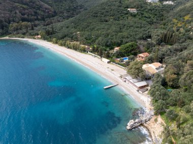 Bu havadan çekimde turkuaz suların kumlu bir sahile ulaştığı evler ve yoğun yeşil bitki örtüsüyle kaplı bir plaj sergileniyor. Manzarası güzel..
