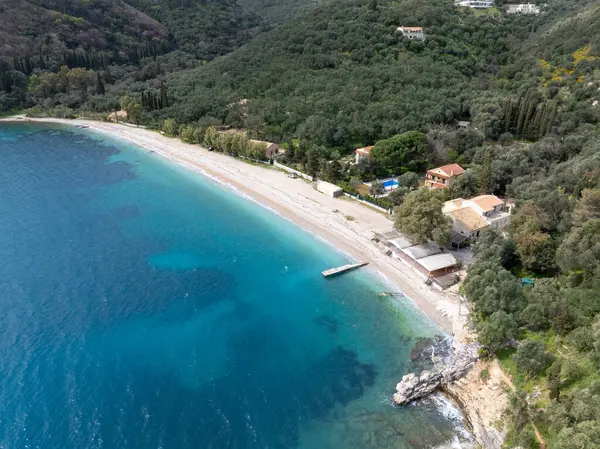 Bu havadan çekimde turkuaz suların kumlu bir sahile ulaştığı evler ve yoğun yeşil bitki örtüsüyle kaplı bir plaj sergileniyor. Manzarası güzel..