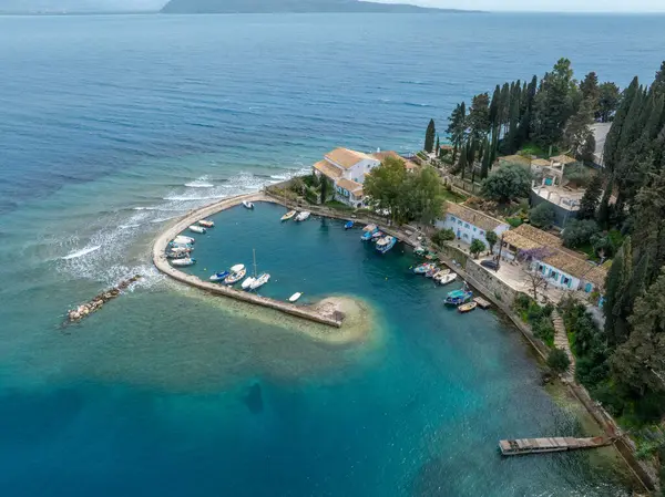 Sahil boyunca binalar ve yemyeşil alanlarla çevrili turkuaz sularda dinlenen sakin bir liman manzarası..