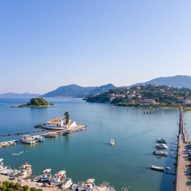 Resmedilmeye değer bir kıyı manzarası sakin turkuaz sular, benekli tekneler, binalı bir ada ve parlak gökyüzünde bir uçak..