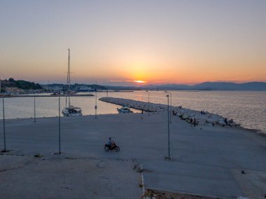 Korfu, korfu, Yunanistan. 15 Ağustos 2020: Yalnız motorsikletli bir Yunan limanının üzerinde gün batımı.