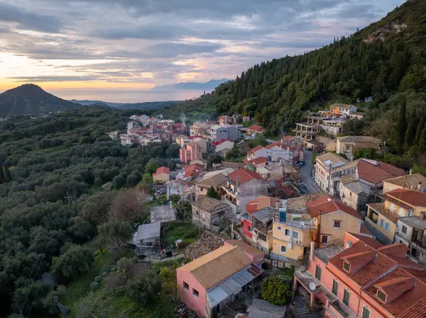 Yüksek açılı bir çekim renkli evleri olan, Alacakaranlık 'ta uzak bir denizi gören yeşil bir yamaçta birleşen antika bir köy sunar..