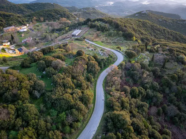 Canlı, yeşil bir yamaçtan geçen ve binaları doğal manzaranın güzelliğine bağlayan bir yolun havadan görünüşü..