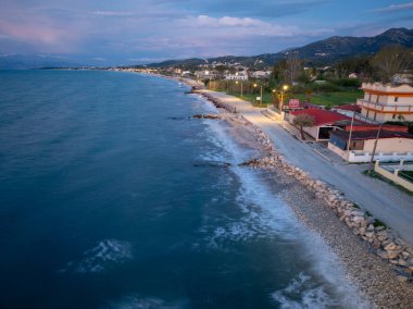 Okyanusun karayla buluştuğu kıyı şeridi boyunca uzanan bir kıyı köyü. Dağlar alacakaranlık gökyüzünün altında kaybolur.. 