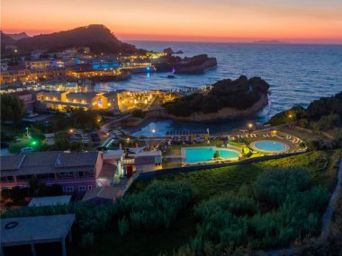 Sakin akşam atmosferinde aydınlık binalar, havuzlar ve okyanus manzaralı büyüleyici bir sahil köyünü yakalıyor..