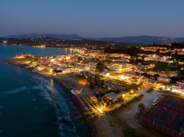 Bu hava manzarası, alacakaranlıkta ışıldayan canlı bir kıyı kasabasını yakalıyor. Huzurlu bir okyanusun yanında, ışıklar sıcak bir ortam yaratır..