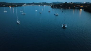 Yukarıdan yakalanan pek çok yelkenli sakin, mavi körfezde dinleniyor. Uzak kıyı şeridi ışıkları güzel bir akşamda parıldıyor..