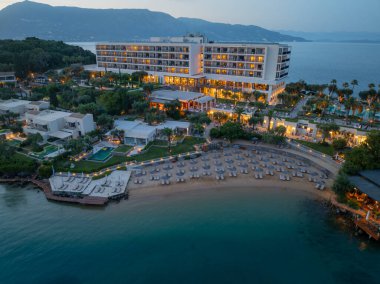 Alacakaranlıkta lüks bir otel, sahil ve dağ sırasının manzarası. Parlak binaları ve kumlu plajları olan çarpıcı bir sahil bölgesi..