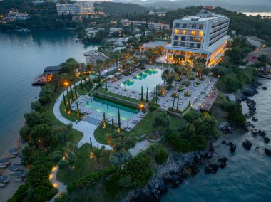 Yüksek açılı bir çekimde birden fazla havuzu, olgun peyzajı ve çağdaş bir oteli olan bir otel sergileniyor. Tatil köyü kıyı şeridiyle kesişiyor..