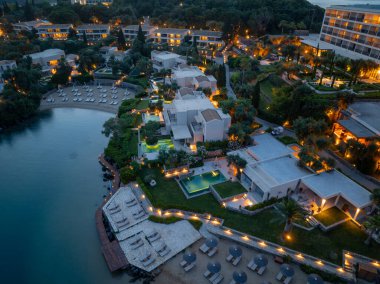 Gece vakti hava manzarası birçok havuzu, villası, aydınlık yolları ve kıyı şeridinde kumlu bir plajı olan lüks bir tatil köyünü gösteriyor..