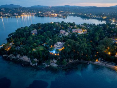 Gecenin büyüleyici ışığı altında sakin sularla çevrili güzel bir adada ağaçların arasında yuva yapmış villaların havadan görüntüsü..