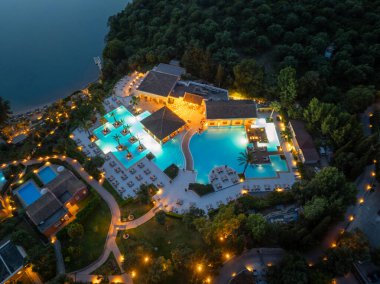 Tepeden çekilen bir görüntü, geceleri, aydınlık havuzlar, güzel binalar ve deniz kıyısındaki yemyeşil ağaçların yer aldığı lüks bir tatil köyünü gözler önüne seriyor..