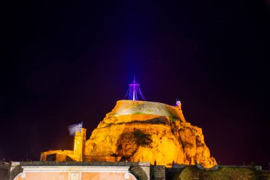 Görüntü, karanlık gökyüzüne karşı mimari detaylarını vurgulayan kayalık bir tepenin tepesindeki aydınlık bir kalenin gece görüntüsünü sergiliyor..