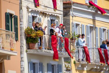Eski binaların balkonlarında toplanan insanları canlı bir sahne, bazıları geleneksel kıyafetlerle süslenmiş kırmızı kumaş dekoru, bir etkinlik için..