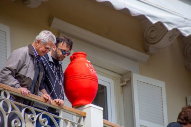 İki adam, biri yaşlı, biri genç biri güneş gözlüklü balkona yerleştirilmiş büyük kırmızı bir kavanozu izliyorlar..