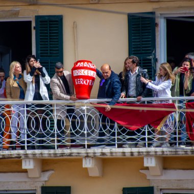 Bir grup balkonda toplanıyor, ellerinde telefonlar, yazılı bir seramik tencerenin etrafında, kültürel ya da toplumsal bir olayı kutluyorlar..