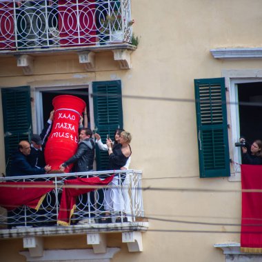 Balkondaki insanlar, büyük, dekoratif bir kavanozu, kutlamayı izleyenlerle birlikte atmak için işbirliği yapıyorlar..