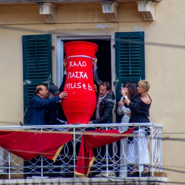 Bir grup insan balkonda toplandı, büyük bir kırmızı tencereyi dikkatle tutuyorlardı, muhtemelen bir kutlama sırasında ya da geleneksel bir olay sırasında.. 