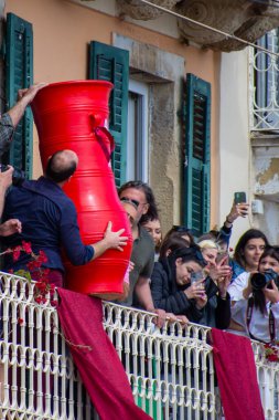Balkondaki kalabalık, insanların festival sırasında büyük kırmızı kaplar atmasını izliyor. İzleyiciler fotoğraf çekiyor ve geleneği belgeliyor..