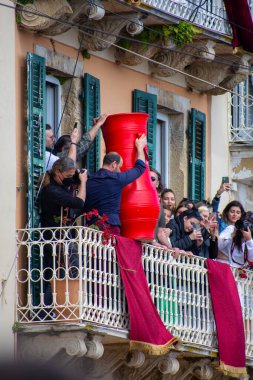 Balkondaki insanlar büyük kırmızı bir vazoyu sokağa atarak kutluyorlar. İnsanlar heyecan verici gösteriyi izleyip fotoğraflarını çekiyorlar..