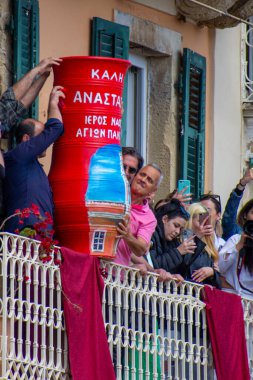 Balkonda elinde büyük kırmızı bir demlik olan insanlar yazı ve bina çizimleri tutarken, diğerleri kutlama sırasında telefonlarıyla kayıt yapıyor..