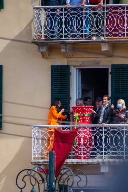 İnsanlar balkondan kutlama yapıyorlar. Büyük, dekore edilmiş bir vazo, pankartlarla birlikte, bayramlık, muhtemelen kültürel bir olayı simgeliyor..