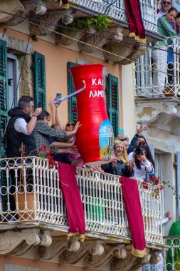 Balkonda heyecanlı bir grup insan, festival sırasında seramik çömlek atarak, etkinliği telefonlarıyla kaydederek kutluyor..