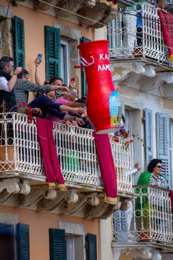 Yunanistan 'ın Korfu kentinde düzenlenen bir etkinlikte büyük, kırmızı bir seramik çömlek fırlatılırken, insanlar balkonlardan izliyor. Kutlama görülebilir..
