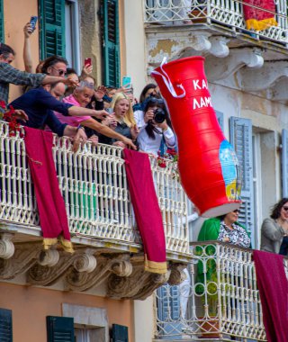 Balkonlardan eğilen, kameralar çekilen, dev bir çömleğin fırlatılışını izleyen neşeli insanların olduğu bir sahne. Binalar şenlik havasına renk katıyor..